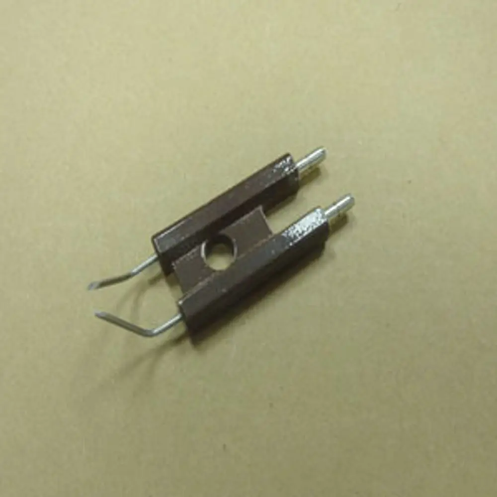 Elektrodenblock mit zwei metallischen Anschlussstiften, auf braunem Untergrund. Produkt von Remeha zur Verwendung in Heizungsanlagen.